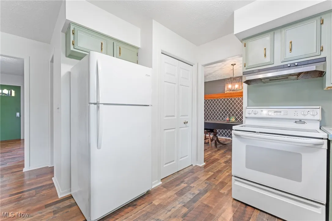 Kitchen with white appliances, a textured ceiling, under cabinet range hood, green cabinetry, and a chandelier