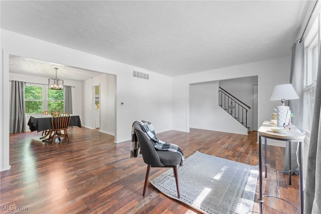 Living room featuring stairway, dark wood finished floors, a textured ceiling, and a chandelier