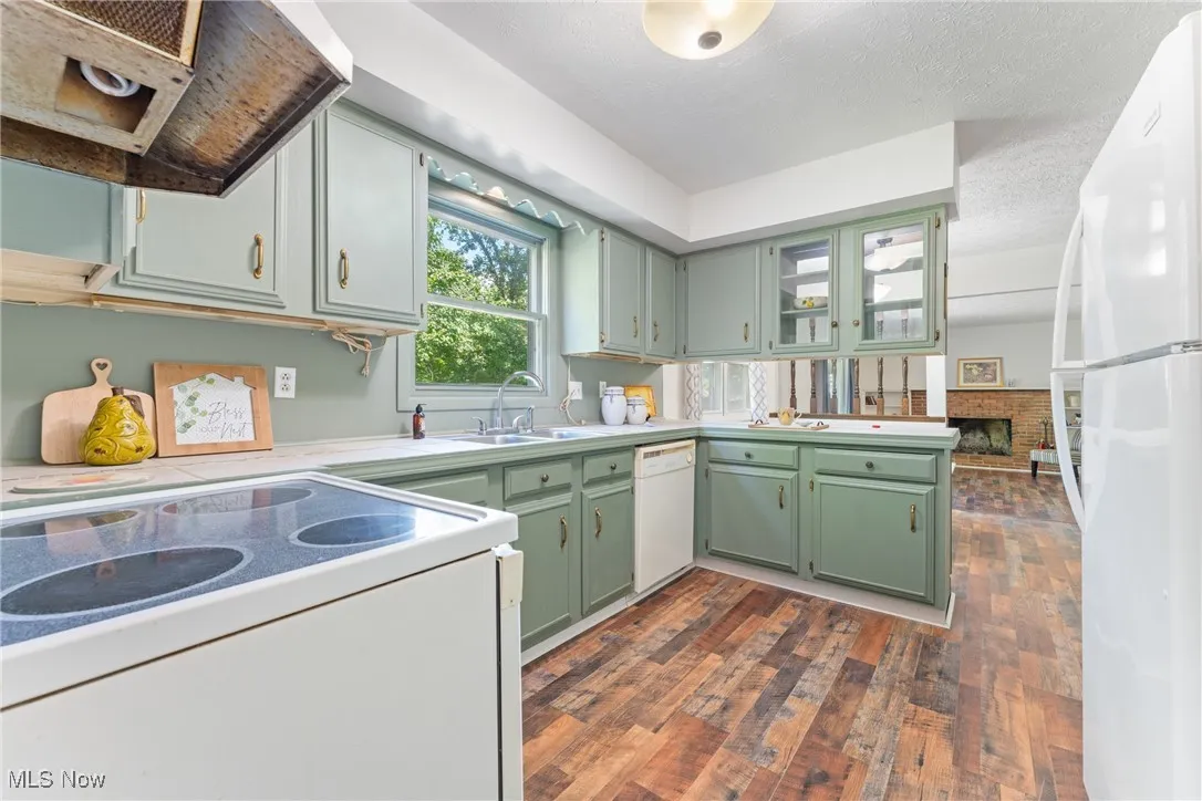 Kitchen featuring white appliances, green cabinetry, extractor fan, a textured ceiling, and dark wood-type flooring