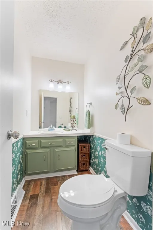 Bathroom with dark wood-type flooring, wallpapered walls, vanity, and a textured ceiling