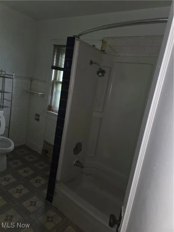 Full bathroom featuring shower / tub combination and tile walls