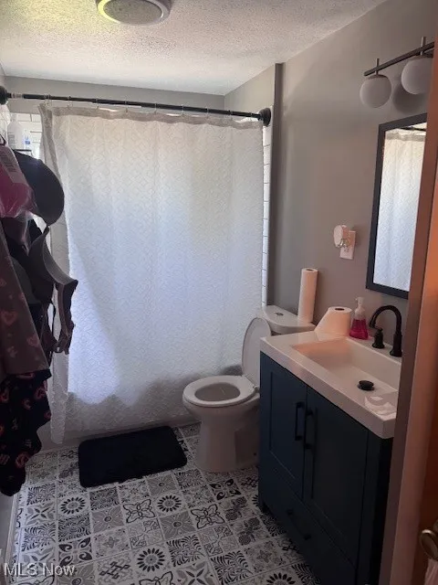 Full bath featuring a textured ceiling, vanity, shower / tub combo with curtain, and light tile patterned floors
