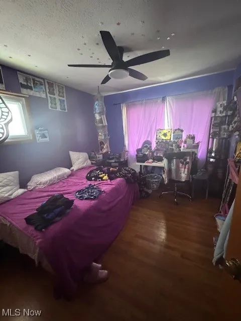 Bedroom with a ceiling fan, dark wood-style floors, and a textured ceiling