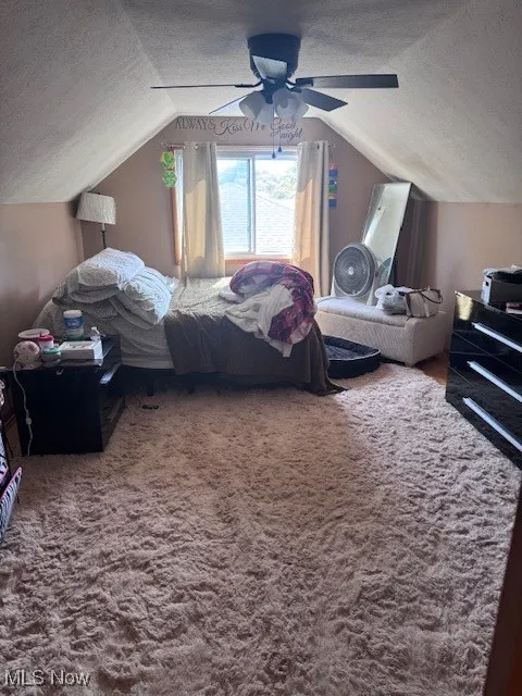 Bedroom featuring a textured ceiling, vaulted ceiling, ceiling fan, and dark colored carpet