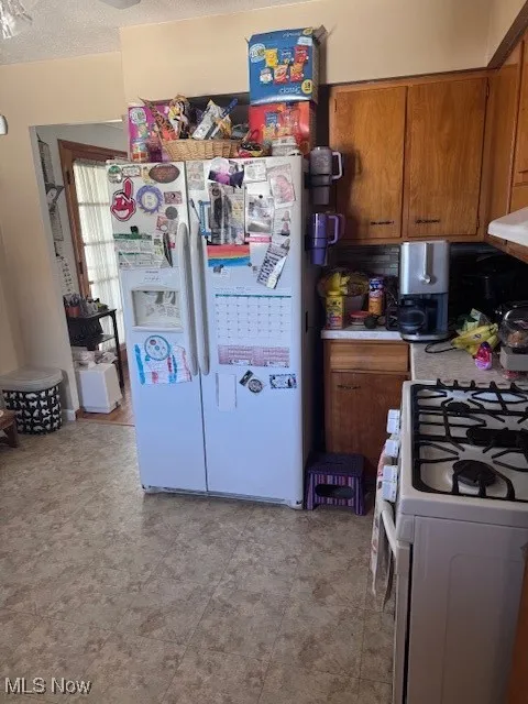 Kitchen with brown cabinets, stove, white refrigerator with ice dispenser, light countertops, and a textured ceiling