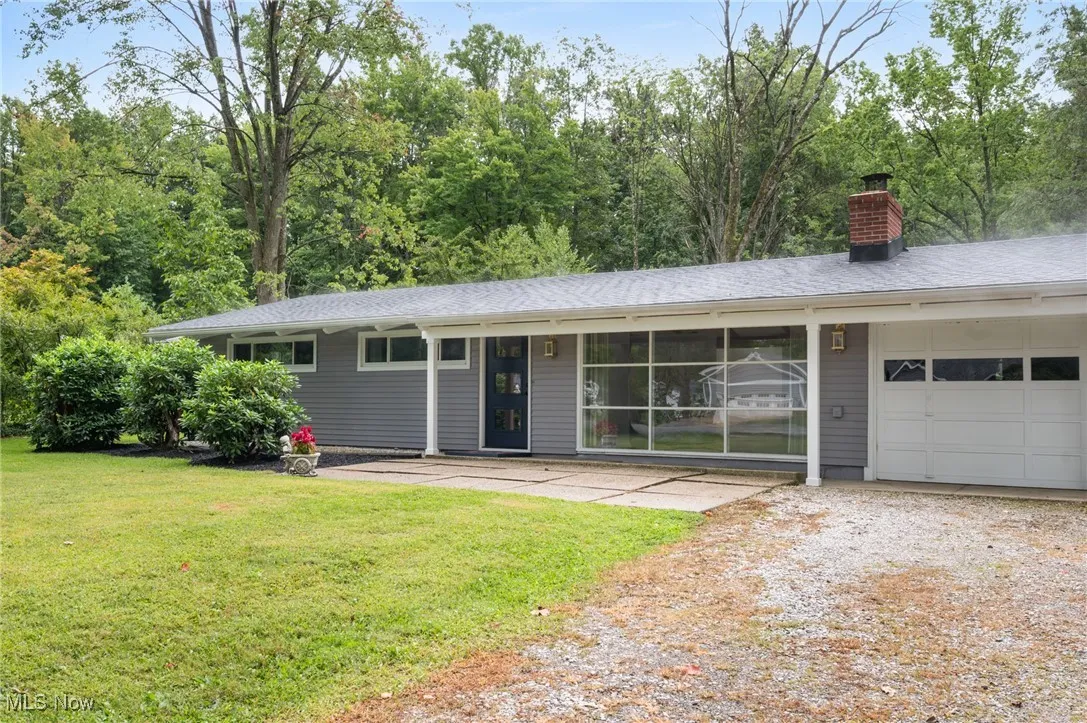 Ranch-style home featuring an attached garage, a chimney, gravel driveway, and a front lawn