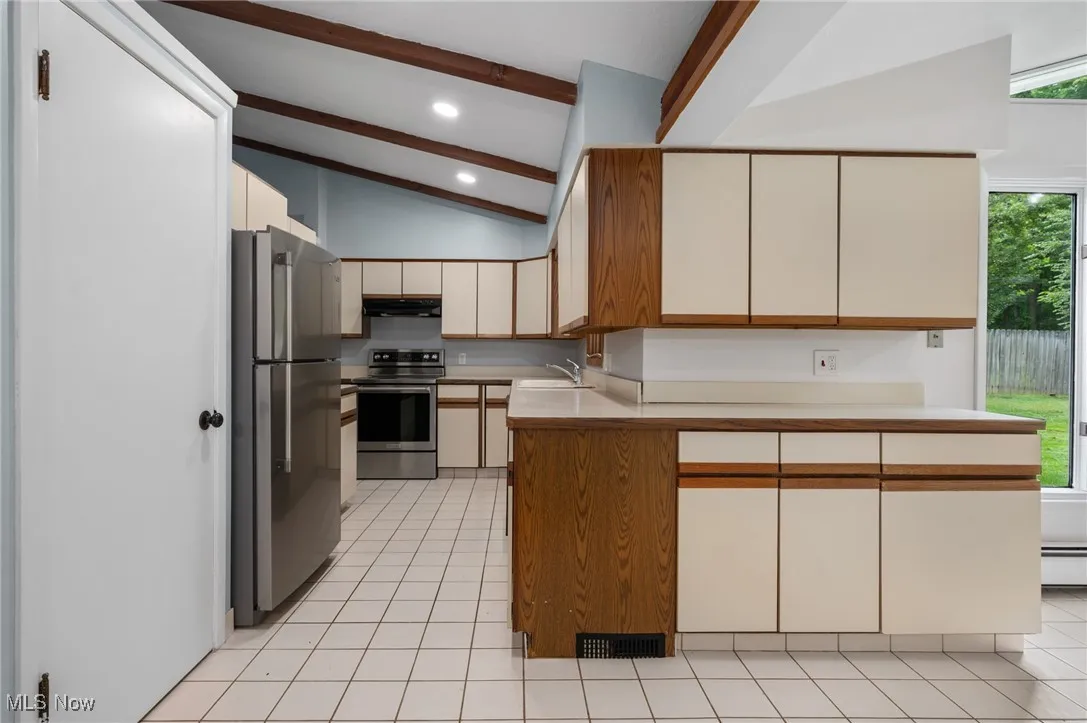 Kitchen featuring stainless steel appliances, light tile patterned floors, brown cabinets, a peninsula, and recessed lighting