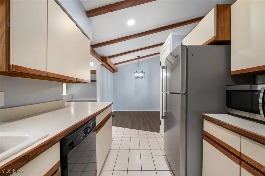 Kitchen featuring pendant lighting, brown cabinetry, light countertops, appliances with stainless steel finishes, and white cabinetry