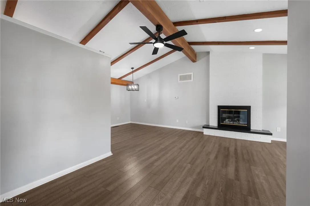 Unfurnished living room featuring a brick fireplace, dark wood-style flooring, a ceiling fan, and a chandelier