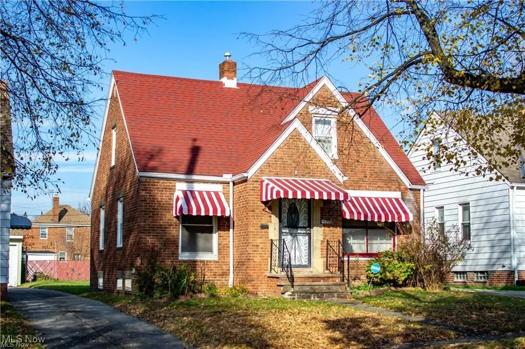 View of front facade featuring a chimney, brick siding, and roof with shingles