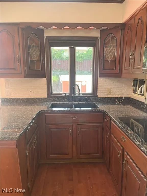 Kitchen with dark wood-type flooring, black electric stovetop, glass insert cabinets, and dark stone counters