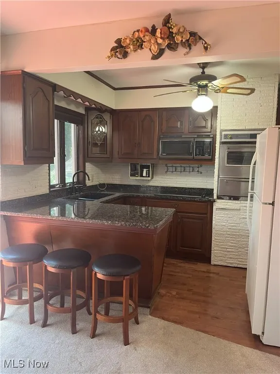Kitchen featuring dark brown cabinetry, freestanding refrigerator, backsplash, and a peninsula