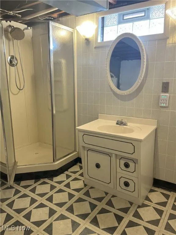 Full bath featuring a stall shower, vanity, and tile walls