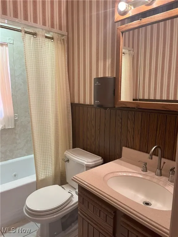 Full bath with shower / tub combo, vanity, wood walls, and tile patterned floors