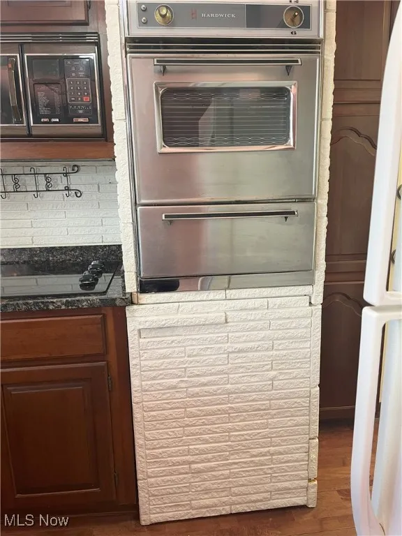 Kitchen featuring oven, black microwave, dark wood finished floors, a warming drawer, and backsplash