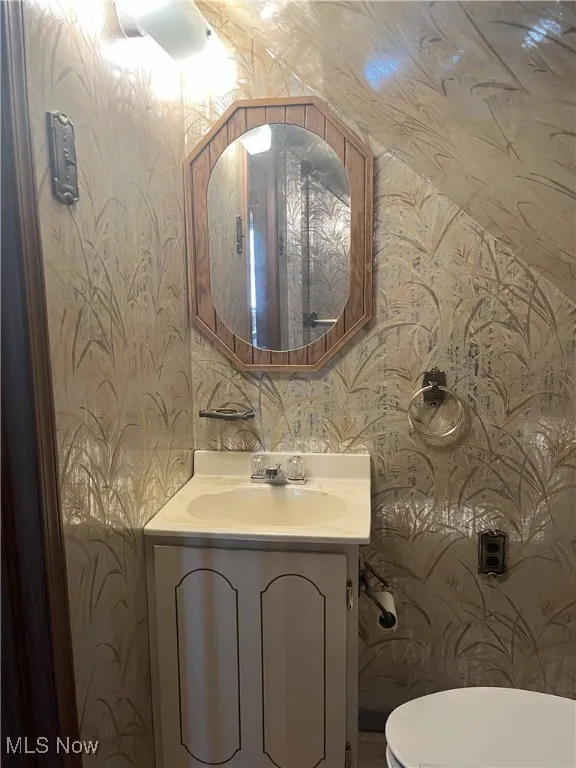 Half bathroom featuring wallpapered walls and vanity