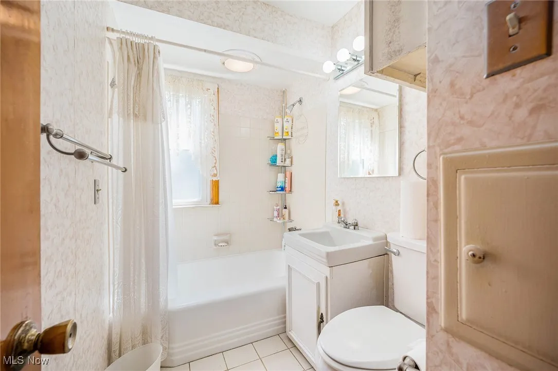 Bathroom featuring shower / bath combo with shower curtain, vanity, wallpapered walls, and light tile patterned flooring