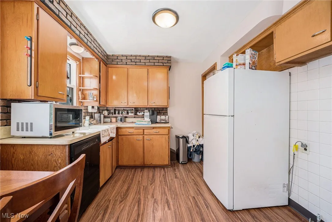 Kitchen featuring open shelves, light countertops, freestanding refrigerator, brown cabinets, and stainless steel microwave