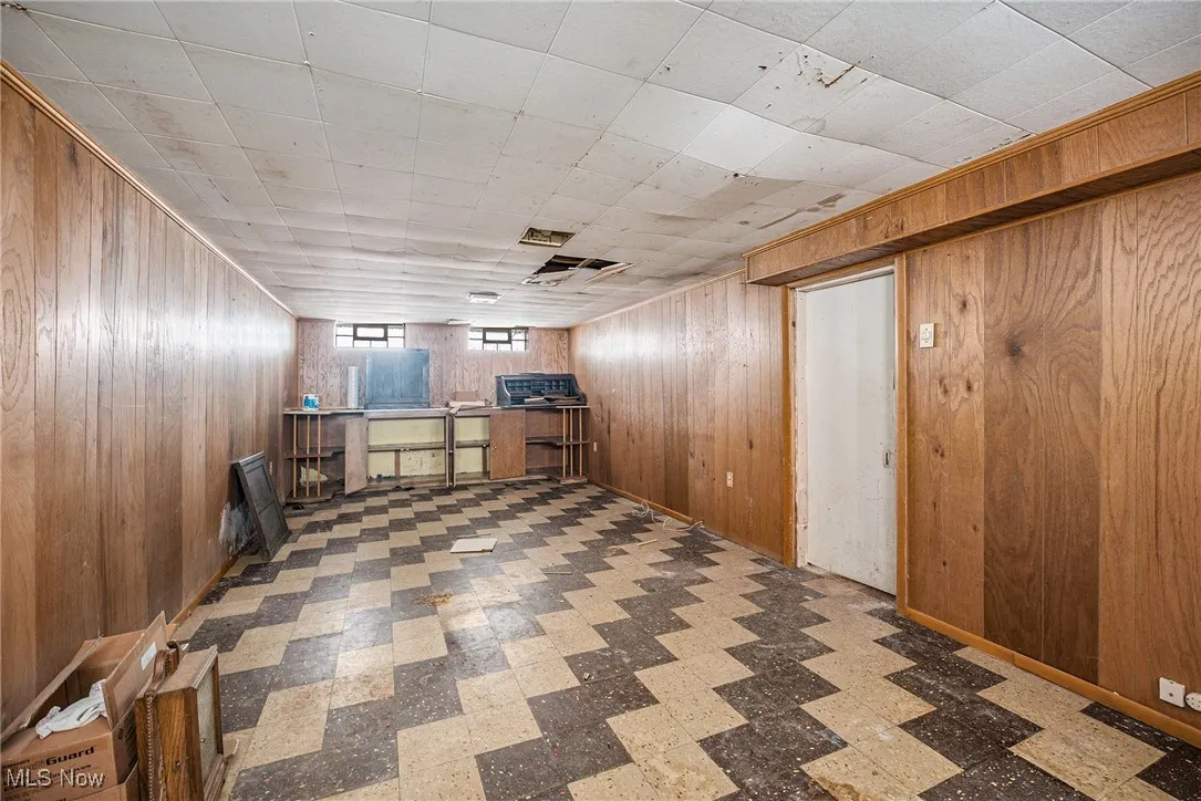 Bar featuring wood walls, light flooring, brown cabinets, and a drop ceiling
