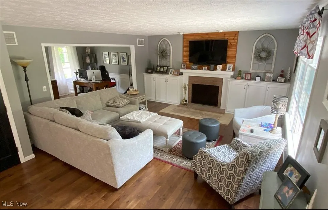Living area with wood finished floors, a textured ceiling, a fireplace, and a desk