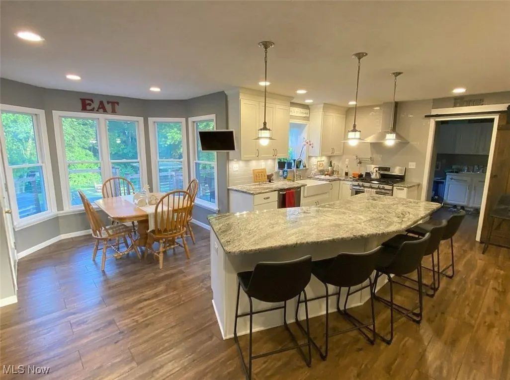Kitchen featuring light stone countertops, a breakfast bar, white cabinetry, stainless steel appliances, and wall chimney exhaust hood