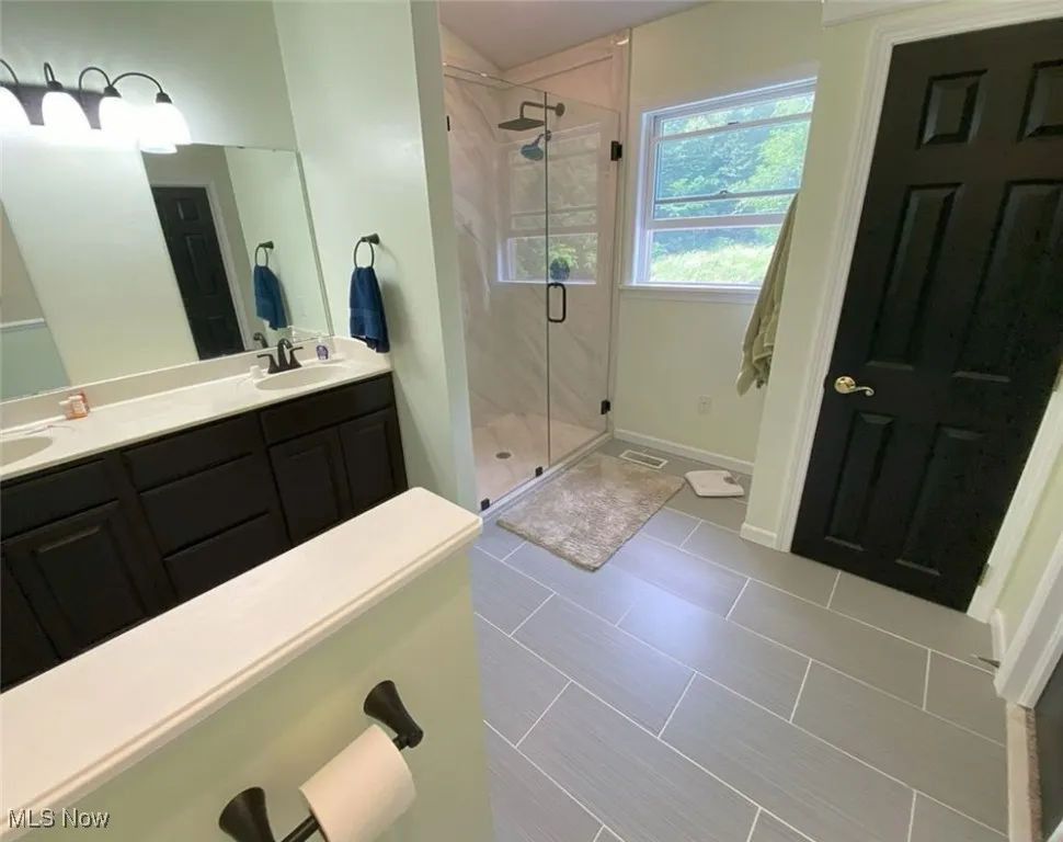 Full bath with a stall shower, double vanity, and tile patterned floors