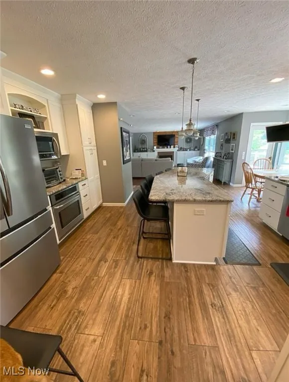 Kitchen featuring open floor plan, white cabinets, stainless steel appliances, light stone countertops, and a textured ceiling