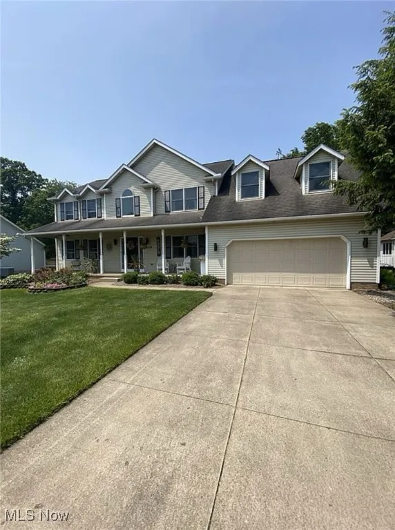 View of front of property with covered porch, driveway, a front lawn, and an attached garage