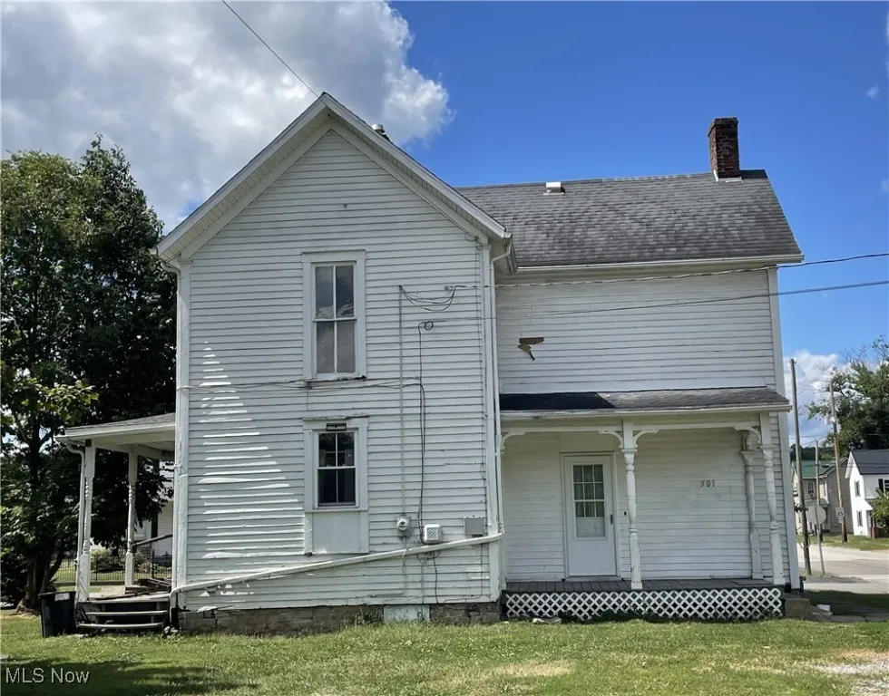 Back view of property with covered porch, a chimney, and a lawn
