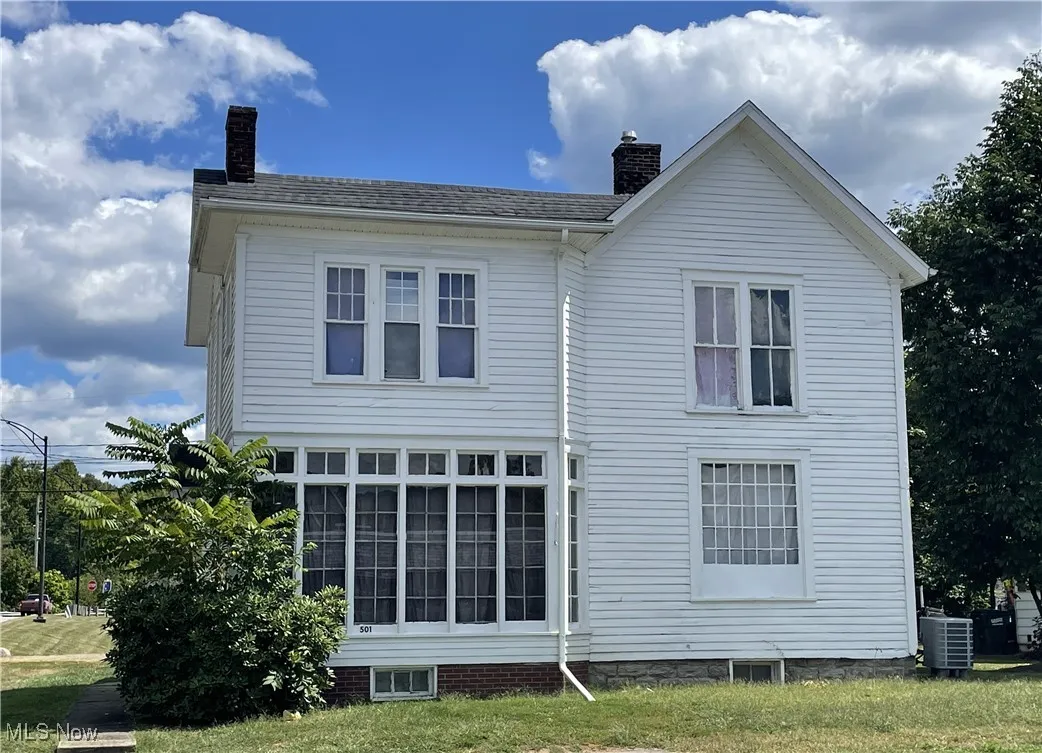 Front of property with a chimney, a shingled roof, and a lawn