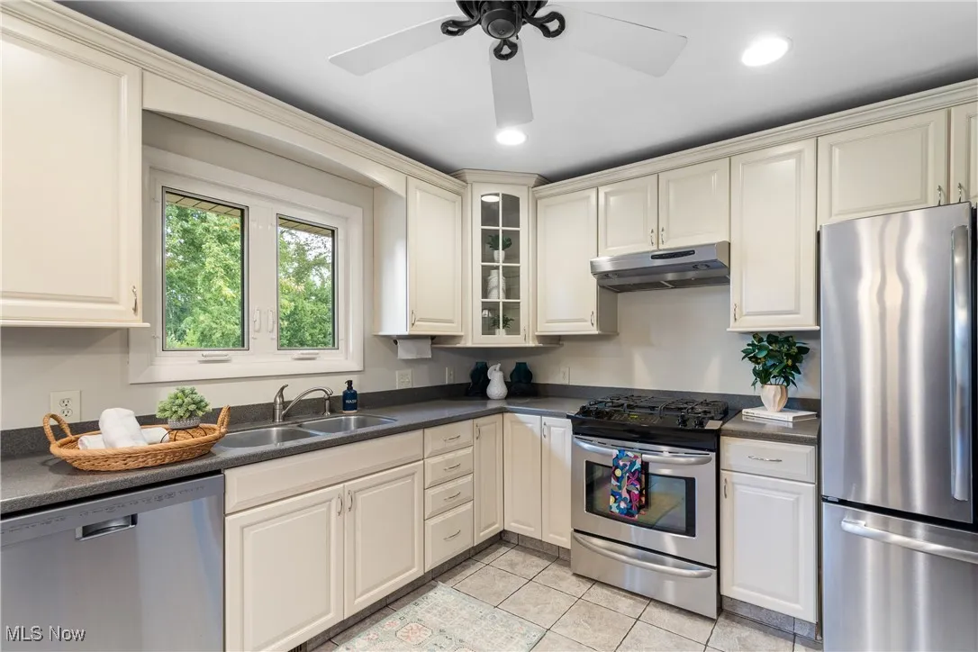 Kitchen with stainless steel appliances, dark countertops, under cabinet range hood, light tile patterned floors, and cream cabinetry