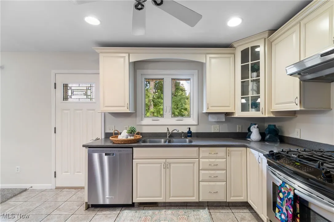Kitchen featuring cream cabinets, gas range oven, dishwasher, dark countertops, and recessed lighting