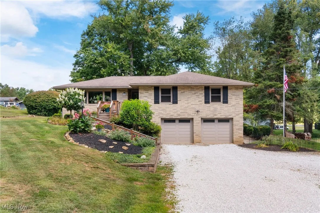 View of front of property featuring brick siding, gravel driveway, a front yard, and an attached garage