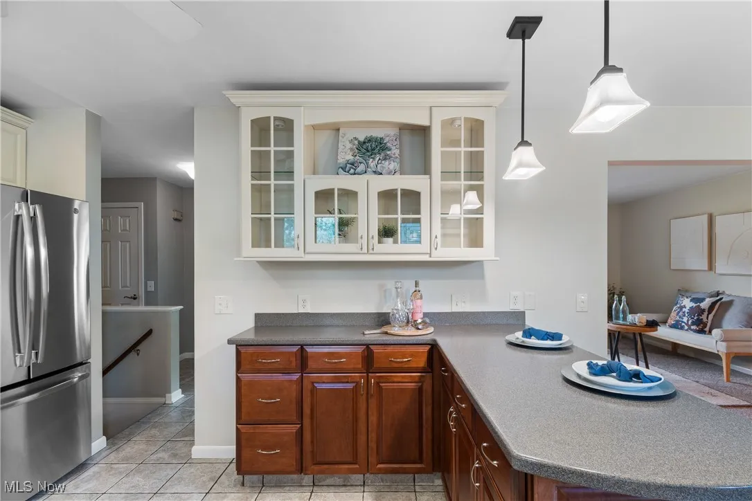 Kitchen with freestanding refrigerator, glass insert cabinets, a peninsula, dark countertops, and decorative light fixtures