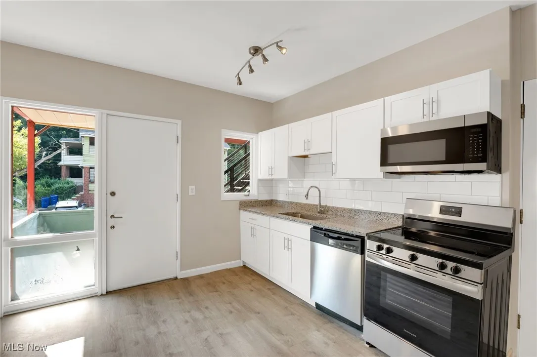 Kitchen featuring appliances with stainless steel finishes, white cabinets, light wood finished floors, and backsplash