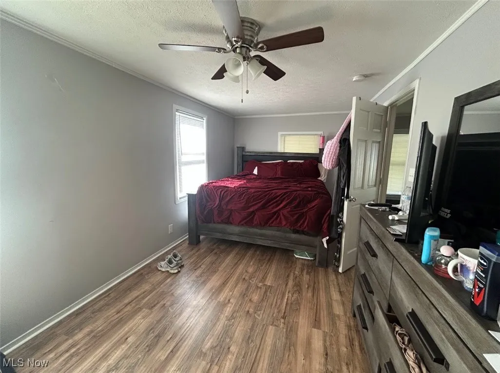 Bedroom featuring a textured ceiling, dark wood-type flooring, crown molding, and ceiling fan