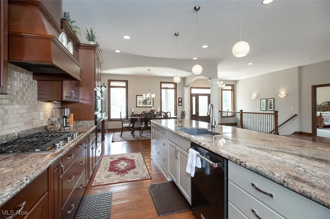 Kitchen with dishwashing machine, light stone countertops, pendant lighting, custom range hood, and gray cabinets