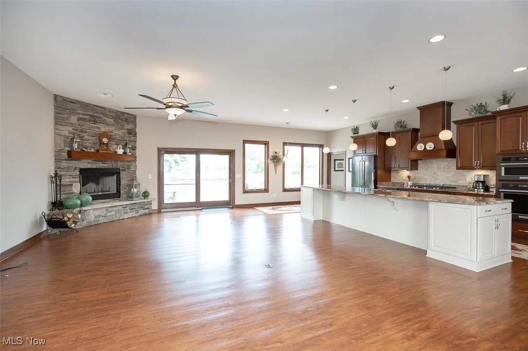 Kitchen featuring open floor plan, backsplash, a kitchen bar, dark wood-style floors, and a stone fireplace