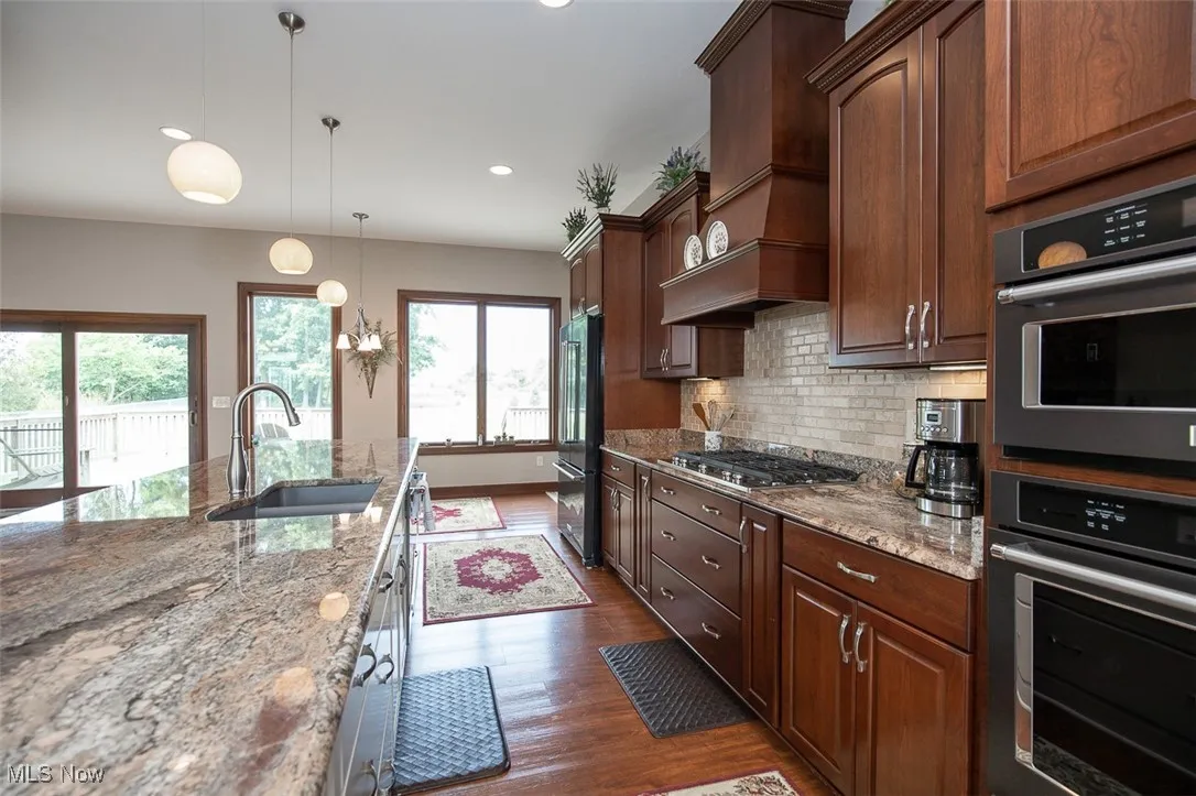 Kitchen featuring light stone counters, hanging light fixtures, decorative backsplash, dark wood-style floors, and appliances with stainless steel finishes