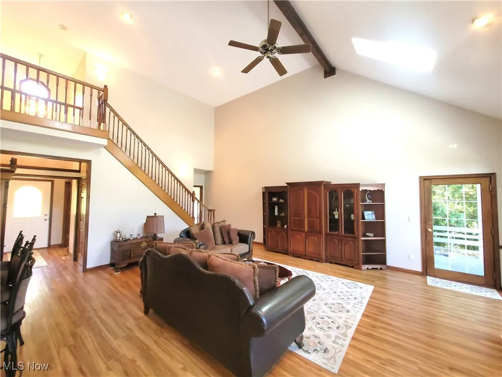 Living room with beam ceiling, high vaulted ceiling, light wood-style floors, a ceiling fan, and stairs