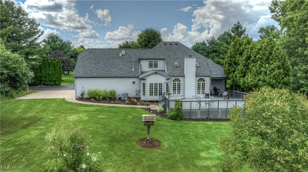 Back of property with a shingled roof, a deck, a lawn, and view of scattered trees