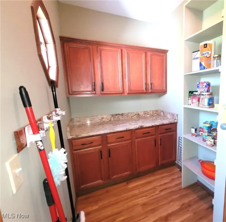 Kitchen featuring light wood-type flooring, brown cabinetry, and light stone countertops