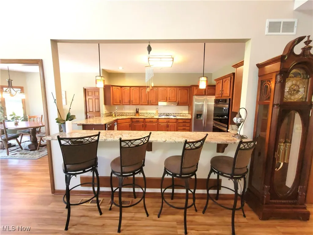 Kitchen featuring brown cabinets, hanging light fixtures, a peninsula, and a kitchen bar