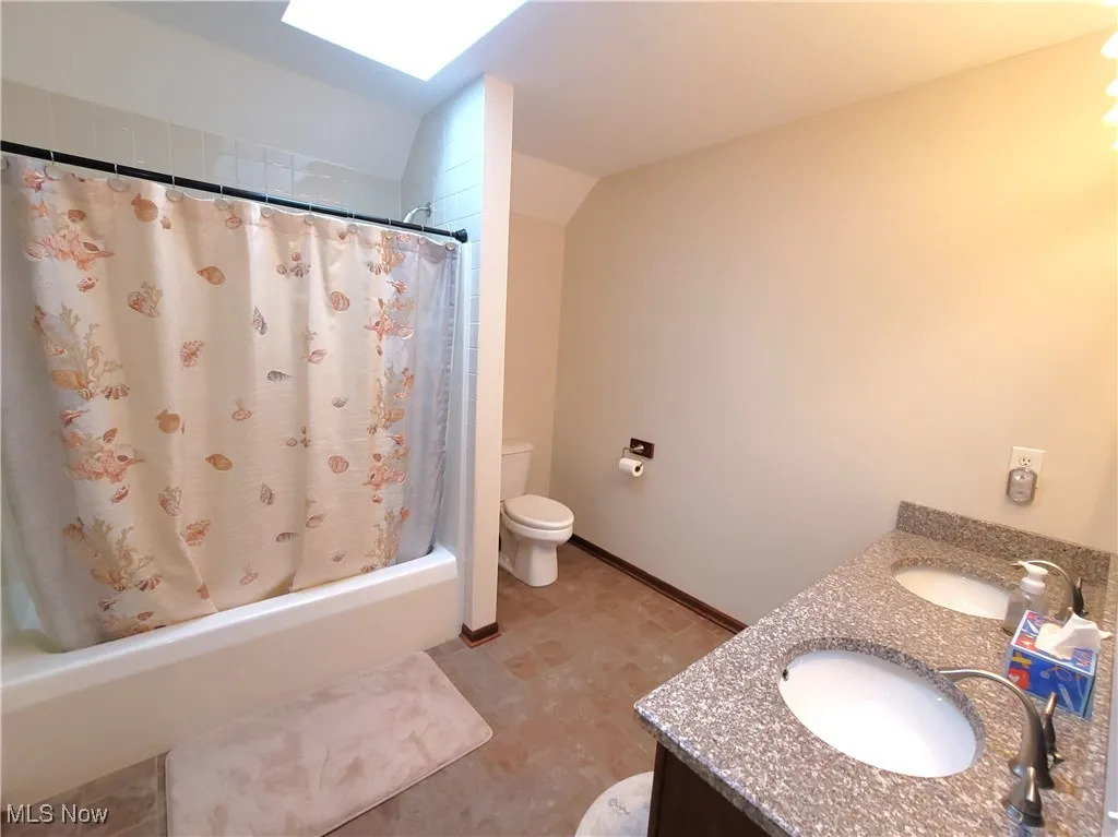 Bathroom with double vanity, lofted ceiling, and shower / bath combo with shower curtain