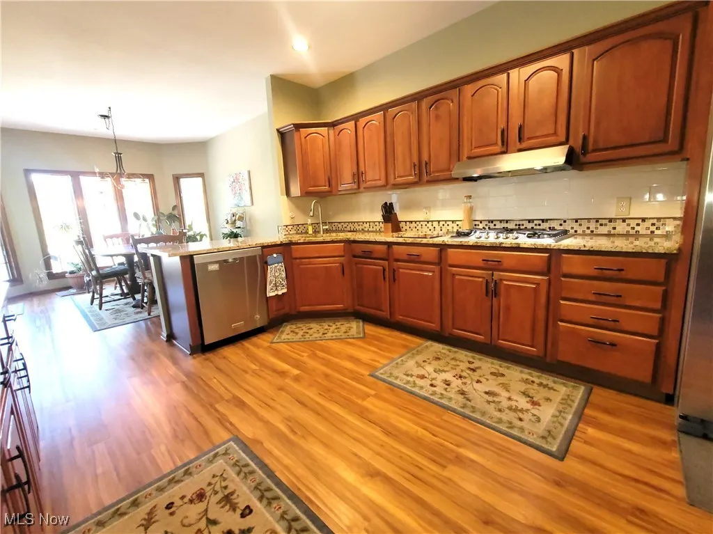 Kitchen featuring a peninsula, decorative light fixtures, stainless steel appliances, brown cabinets, and tasteful backsplash