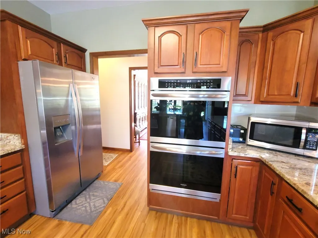 Kitchen with stainless steel appliances, light stone counters, and brown cabinetry