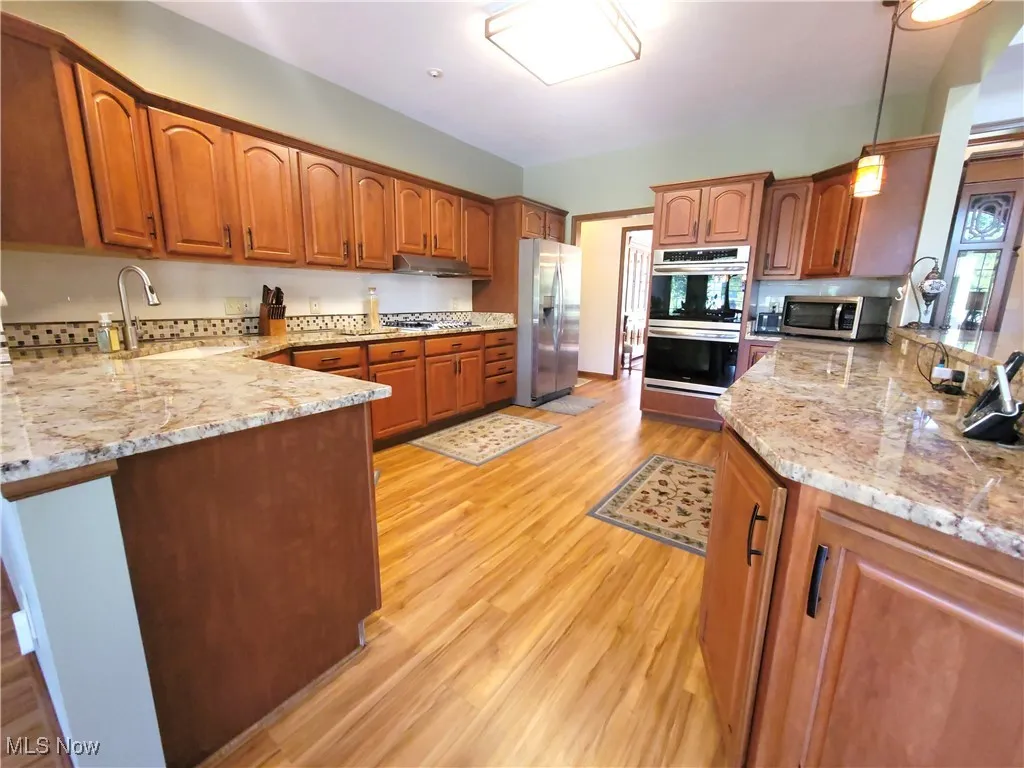 Kitchen featuring brown cabinets, light stone countertops, hanging light fixtures, and stainless steel appliances