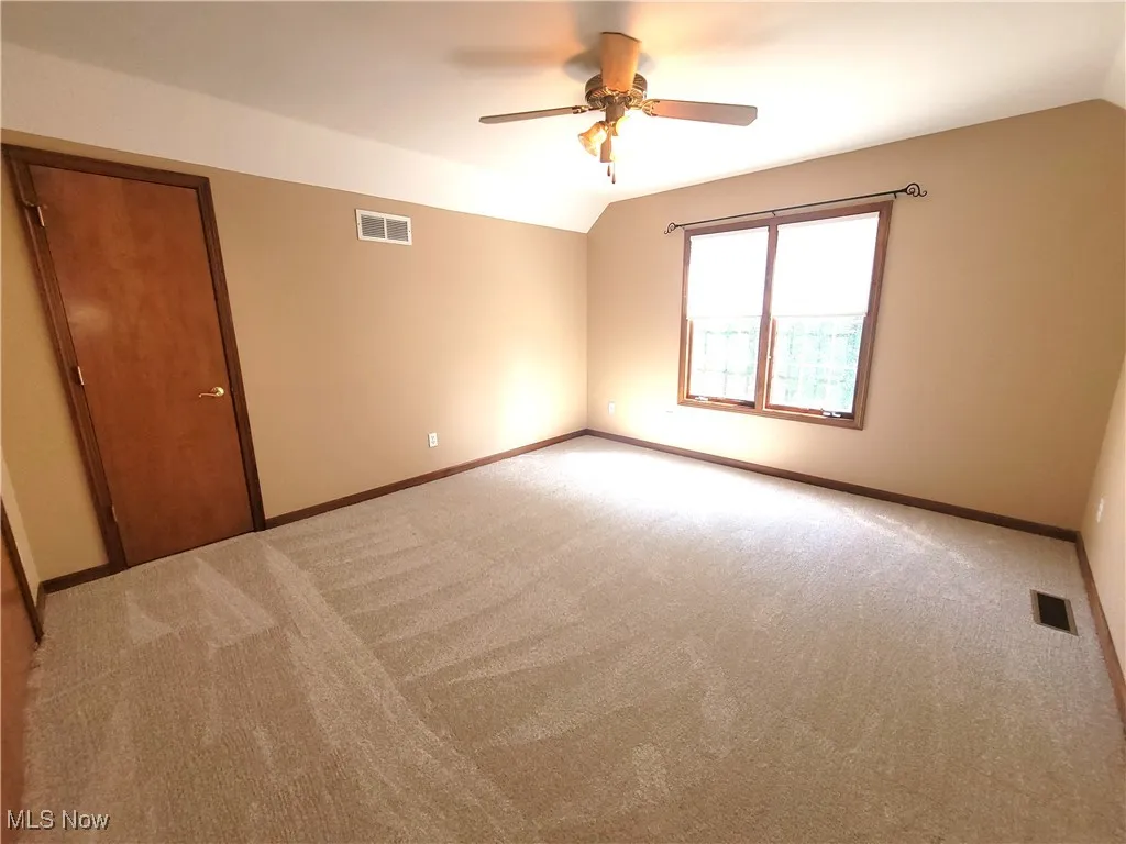 Carpeted empty room with vaulted ceiling and a ceiling fan