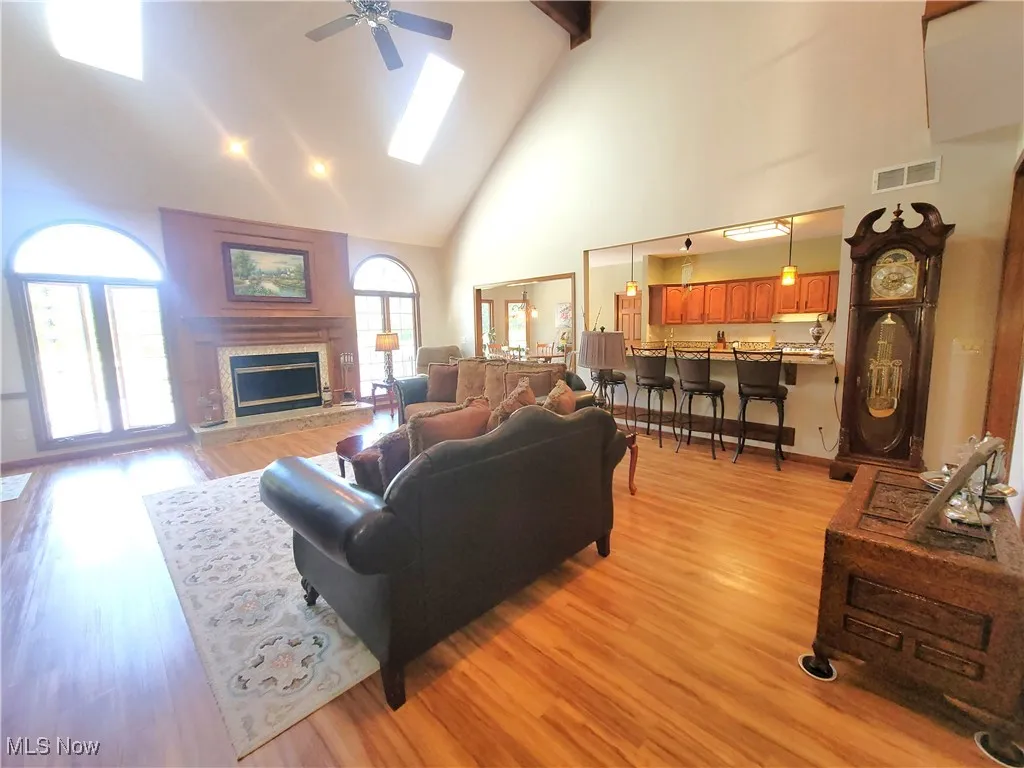 Living room with high vaulted ceiling, light wood finished floors, a skylight, a fireplace, and a ceiling fan