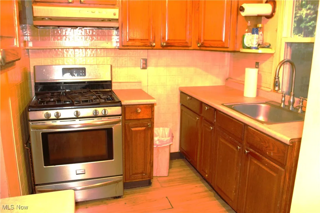 Kitchen with gas range, backsplash, ventilation hood, and light countertops